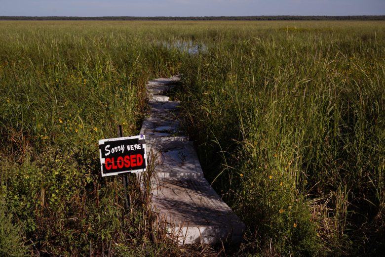 sorry we're closed sign standing next to a boardwalk leading into a grassy wetland field