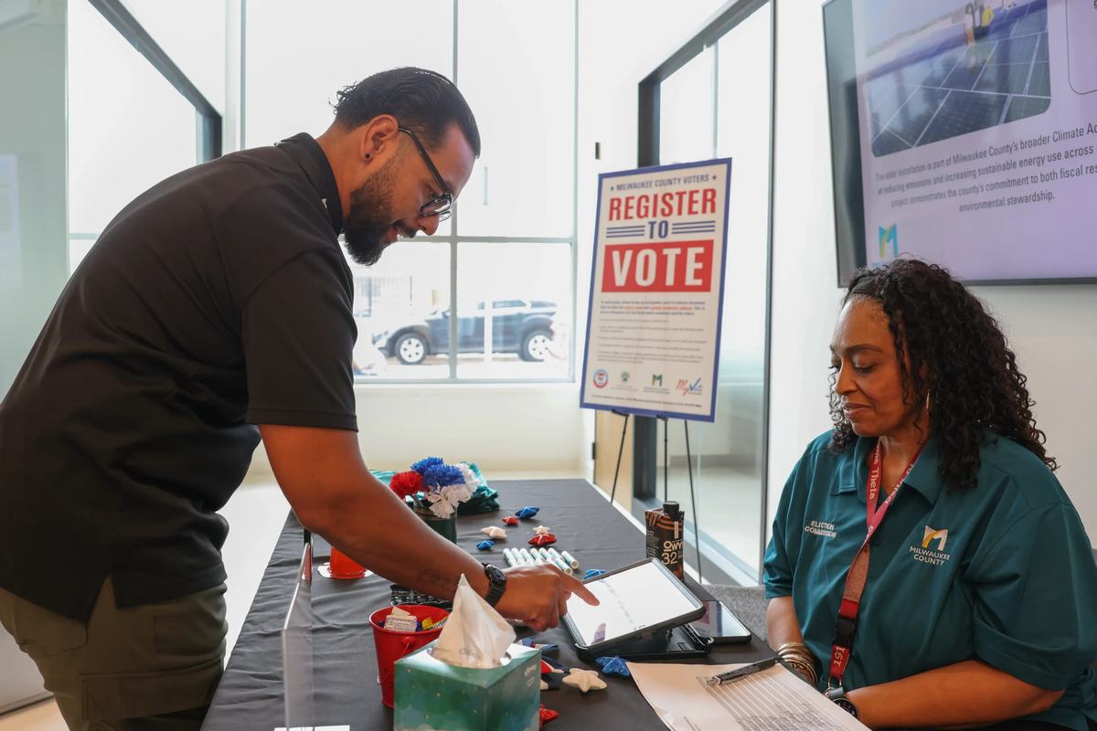 Javier Acevedo talks with Niko Owens, deputy elections director for Milwaukee County, while checking his voter registration status. (Photo by Jonathan Aguilar / Milwaukee Neighborhood News Service / CatchLight Local)