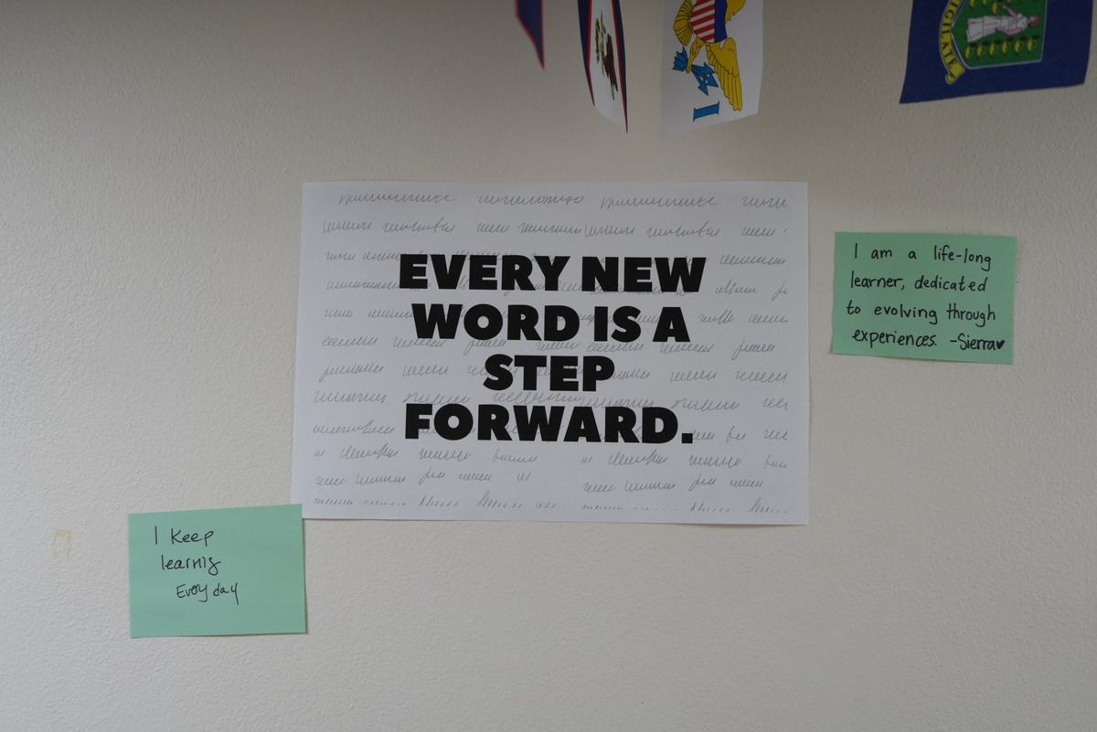 A wall sign reads "EVERY NEW WORD IS A STEP FORWARD" beside notes reading "I keep learning every day" and "I am a life-long learner"