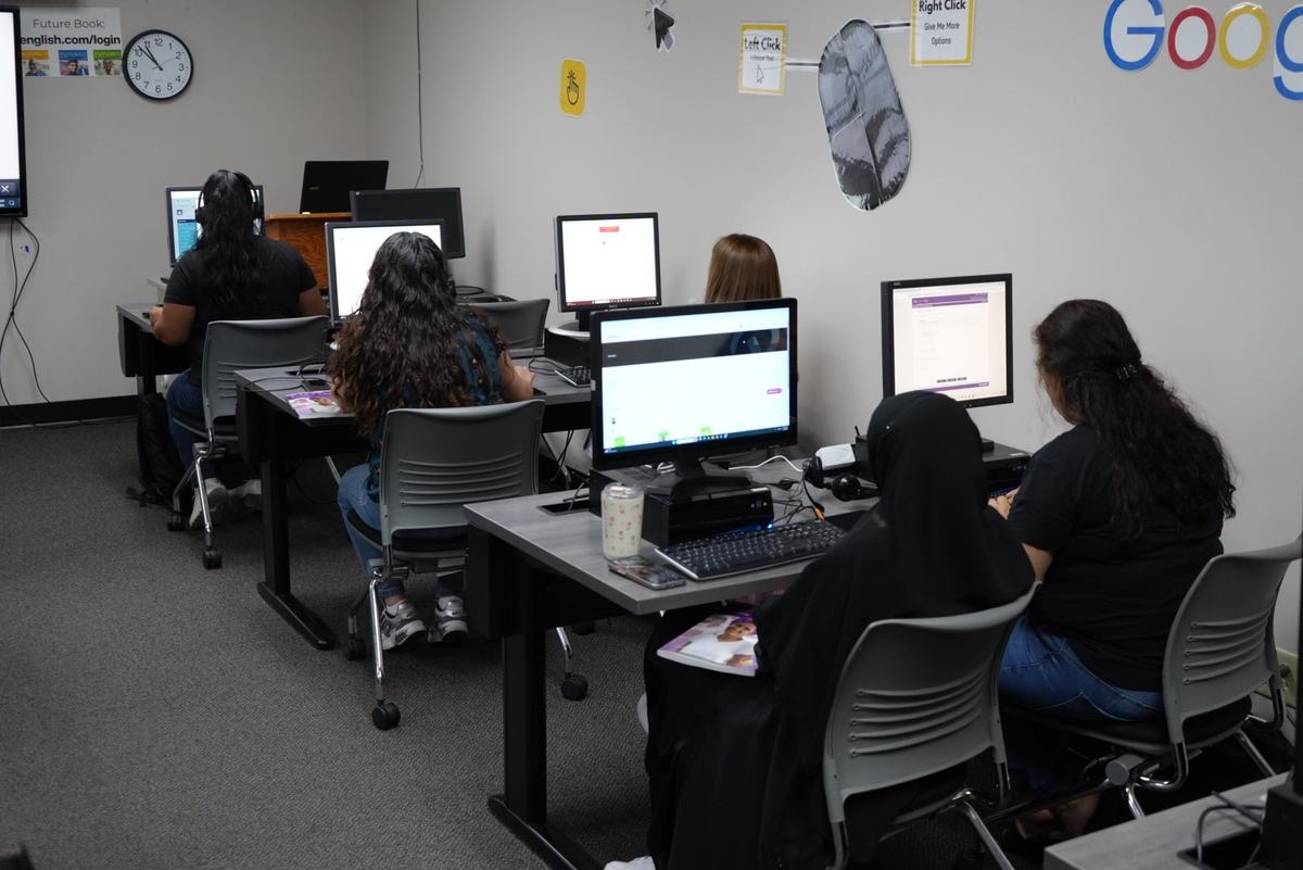 People sit at desktop computers in a room with signs explaining mouse clicks and a web login address on the walls.