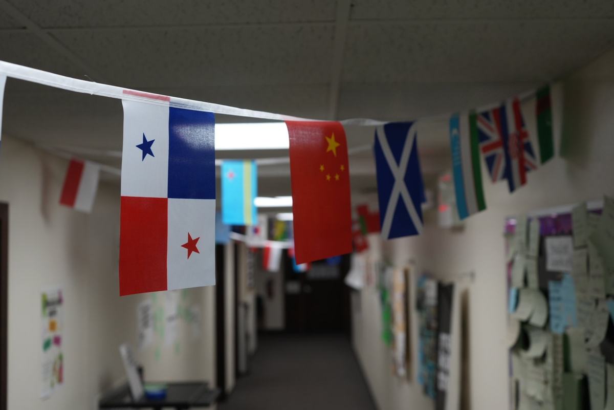 Rows of international flags hang across a hallway with papers posted along the walls.