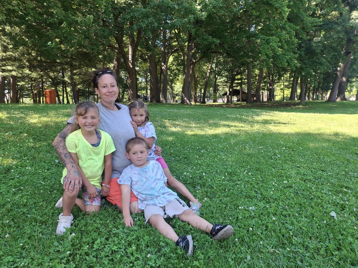 Four people sit together on grass with trees in the background.