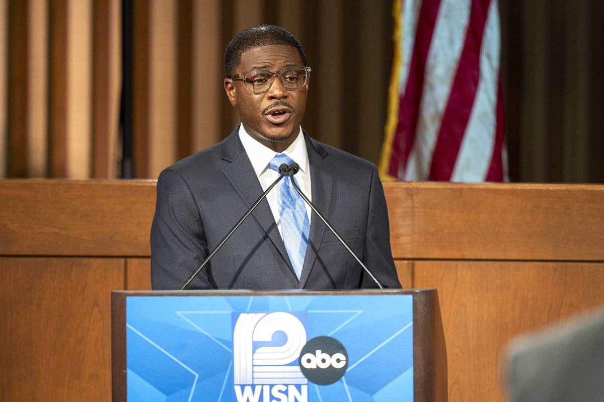 A man in a suit speaks at a podium that says 12 WISN ABC