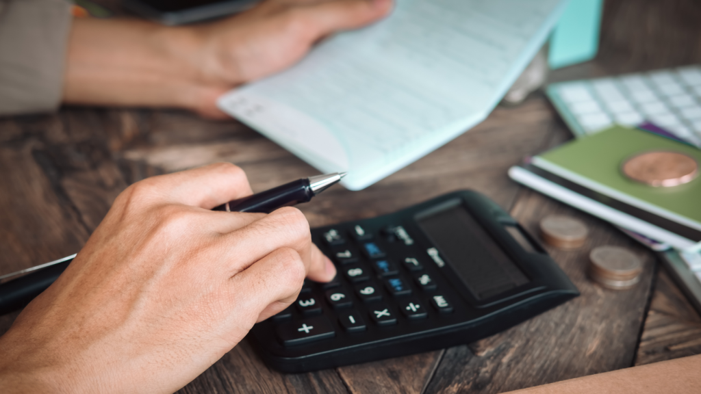 Adding up numbers on a calculator with bills and money nearby. [Stock Photo]
