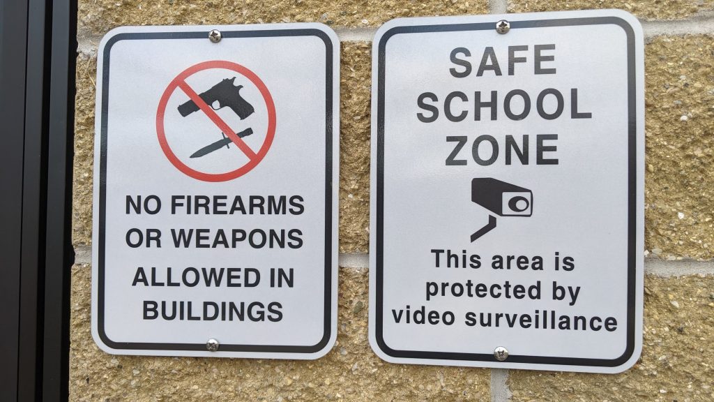 Signs on a school building showing no weapons are allowed, as well as a school safe zone sign.