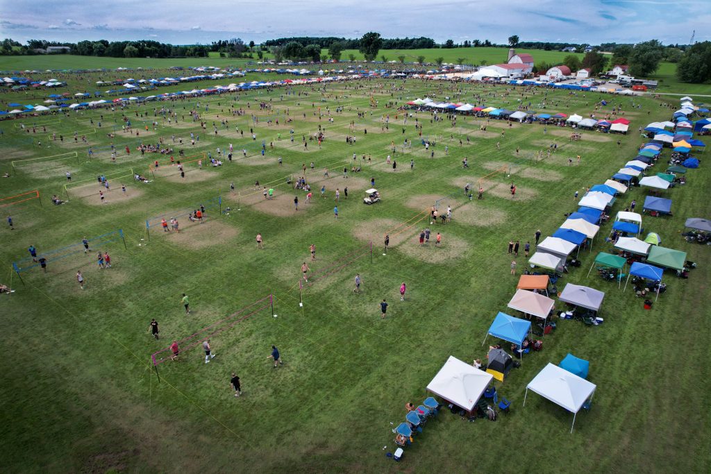 Photo of large field with tents and multiple courts in a grass volleyball tournament.