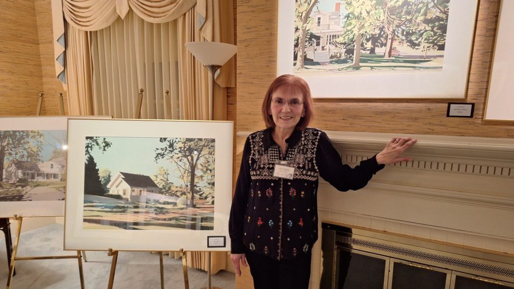 Artist Jody Beighley standing next to her colored pencil drawing of a house.