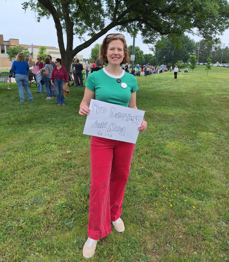 3rd CD Candidate Emily Berge holding a sign that reads Pro Democracy Anti King for USA