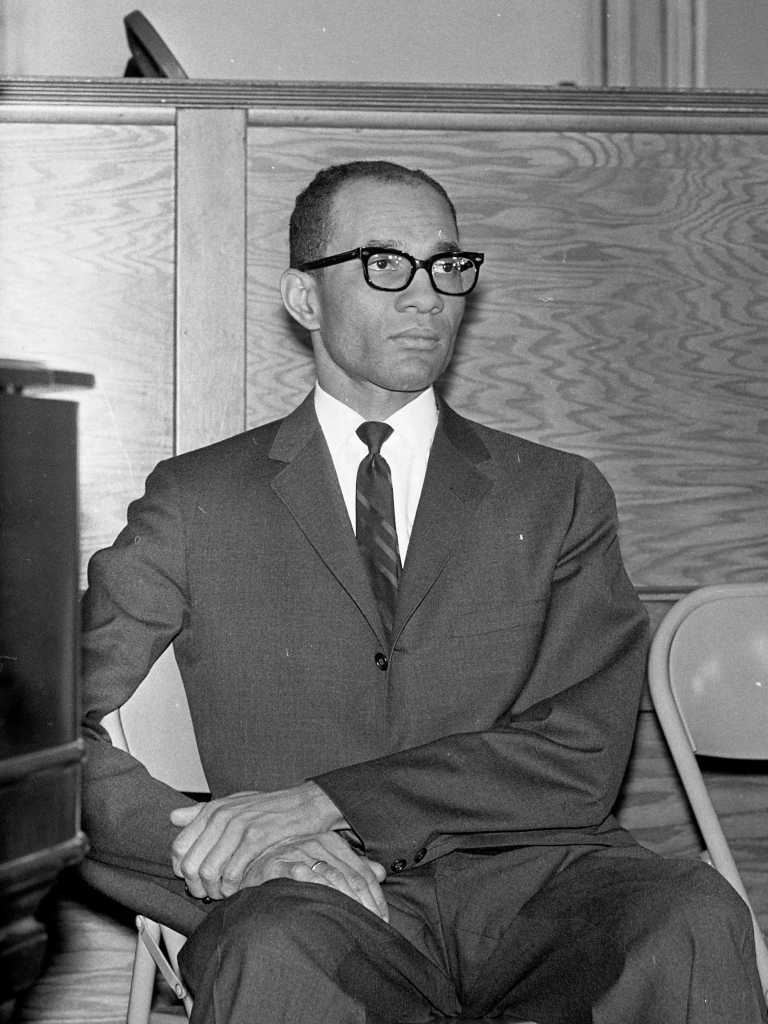 A black and white photograph of Legislator Lloyd Barbee sitting in a folding chair.