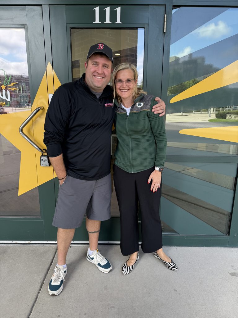 Photograph of Mark Becker with his arm around Secretary of State Sarah Godlewski's shoulder in front of WGBW Studio doors.