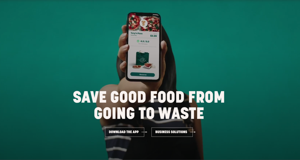Image that says Save Good Food From Going To Waste with a person holding a smartphone showing off the Too Good To Go app.